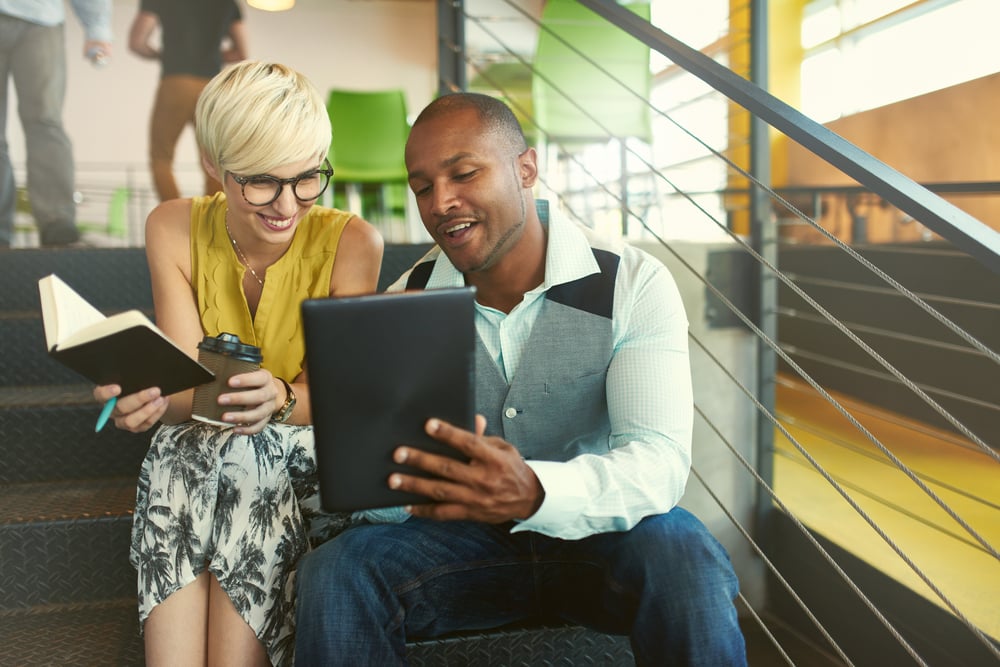 Two creative millennial small business owners working on social media strategy using a digital tablet while sitting on staircase