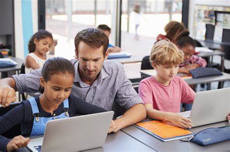 Young teacher helping students on their individual laptops. 